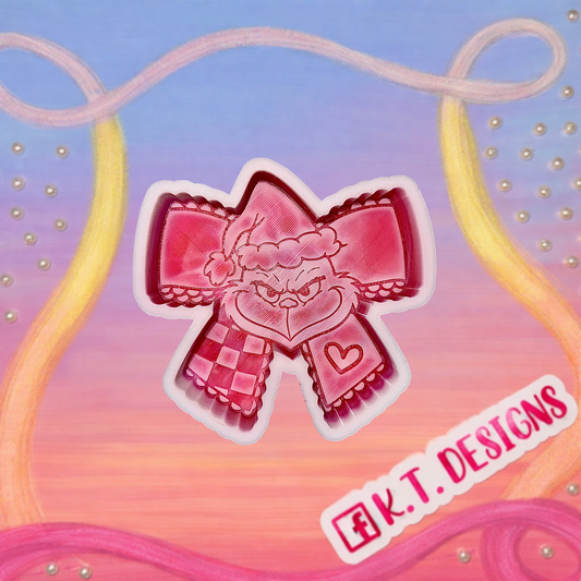 Pink bow car freshie design with decorative elements and a grinch face on a colorful background, featuring the brand 'K.T. DESIGNS'.