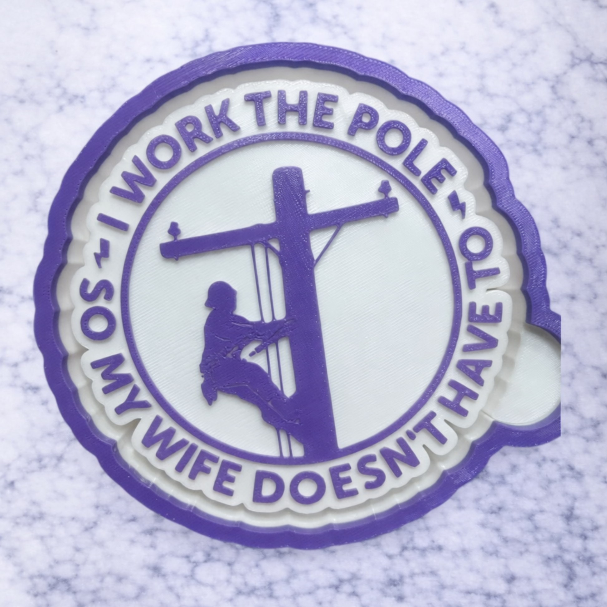 circular car freshie with i work the pole so my wife doesn't have to written in purple with white background. 