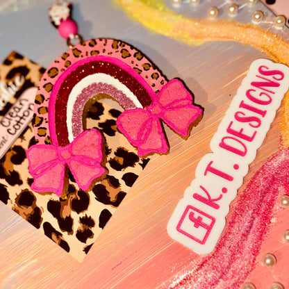 Decorative car freshie with leopard print and pink bows on a colorful background, featuring 'K.T. Designs' branding.