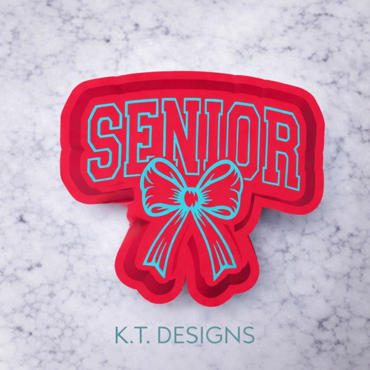 Red and blue 'Senior' freshie mould with a bow on a marble background, branded K.T. Designs.